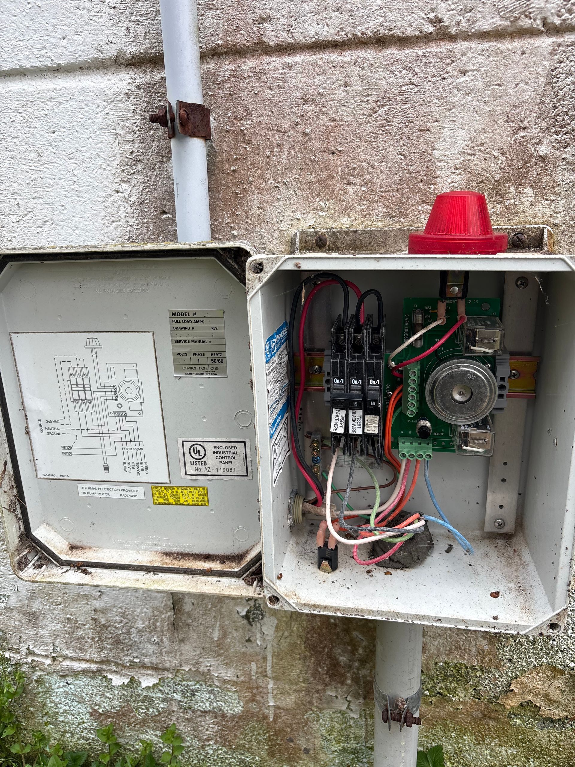 Open electrical control boxes with wiring and red warning light outside a building