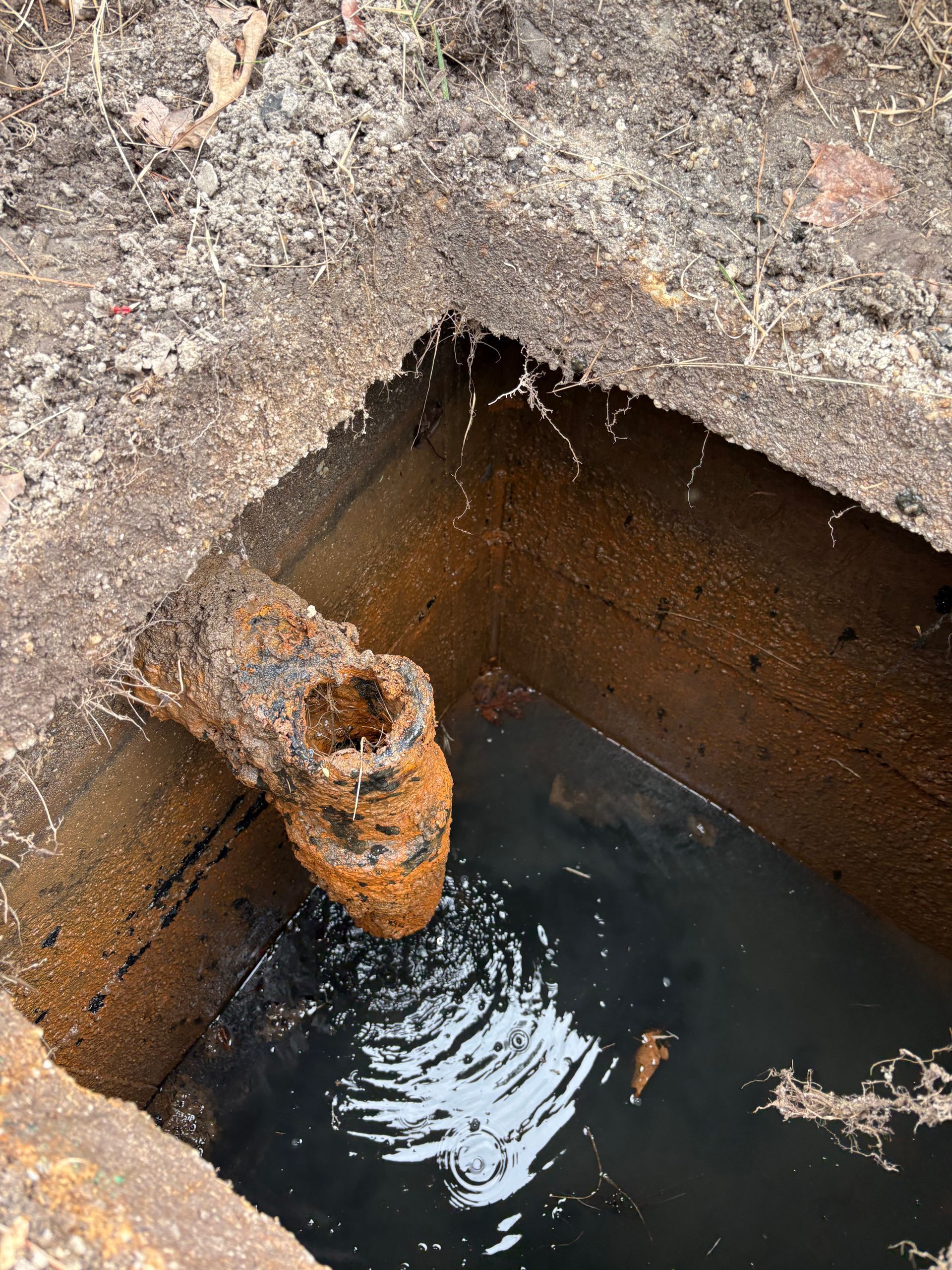 Rusty pipe leaking water into a concrete pit with standing water and ripples