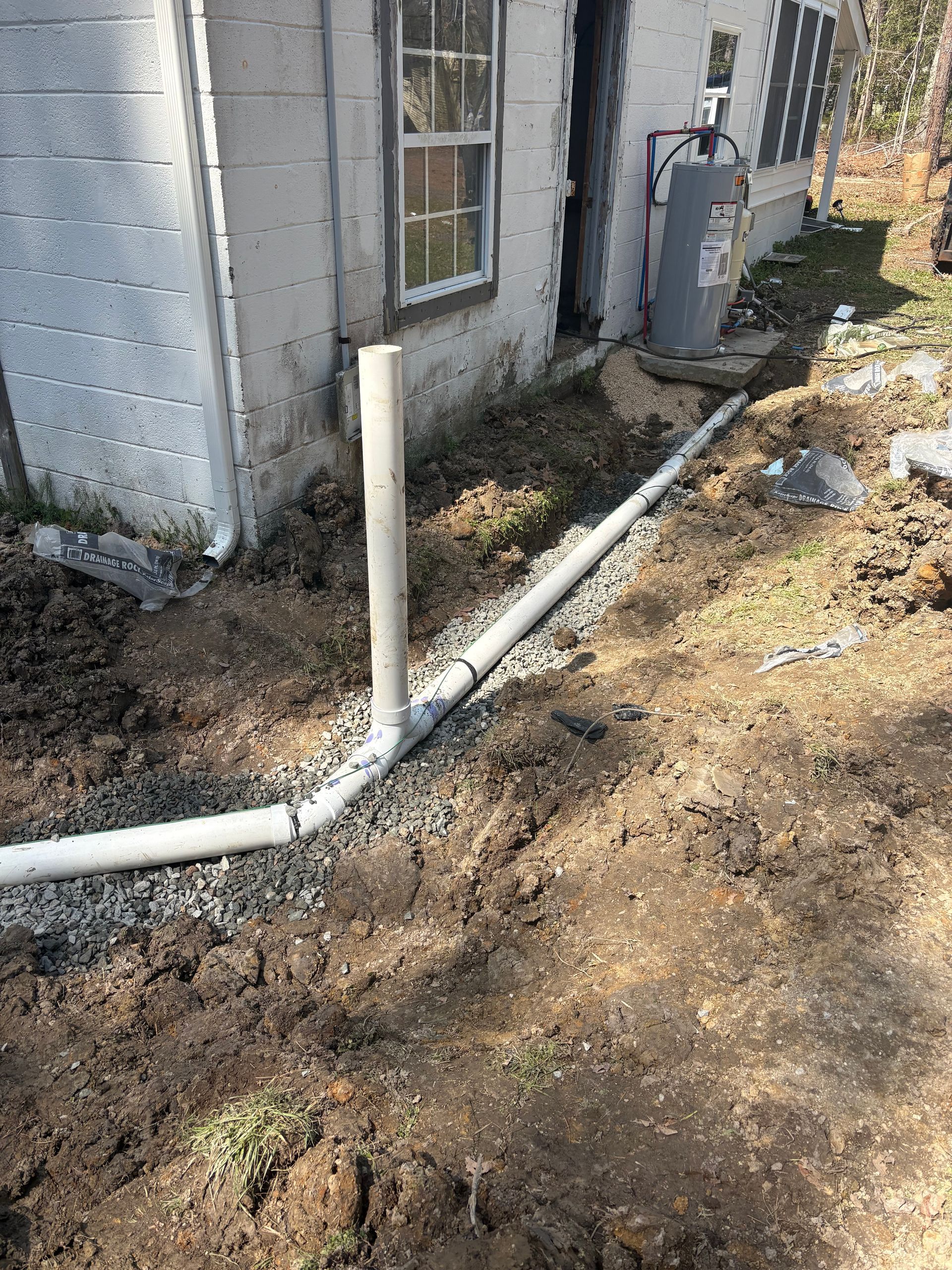 PVC pipes along the side of a cinderblock house near an outdoor utility tank and dirt ground