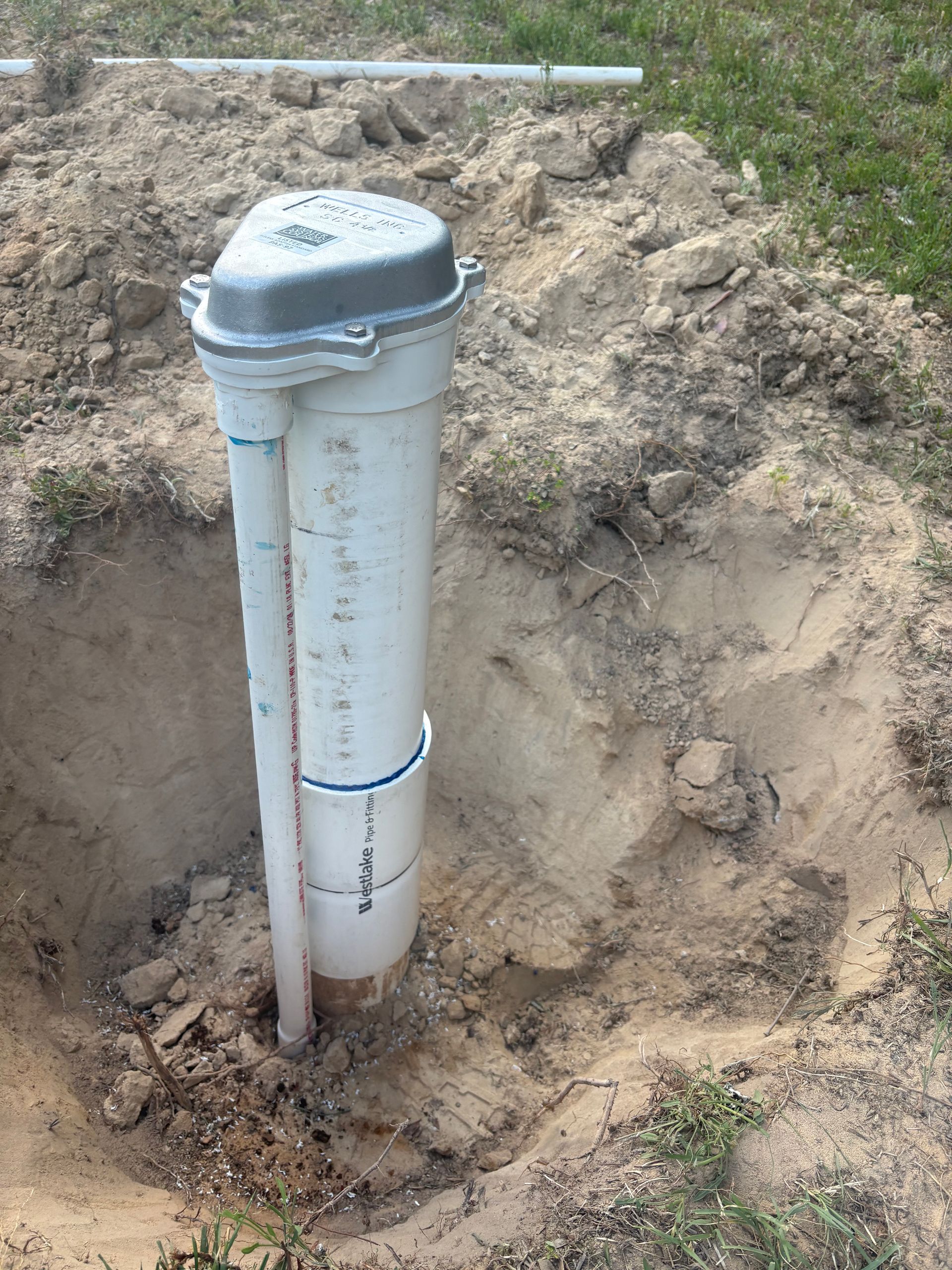 White utility pipe with vent cap installed in a dirt excavation outdoors White utility pipe with vent cap installed in a dirt excavation outdoors