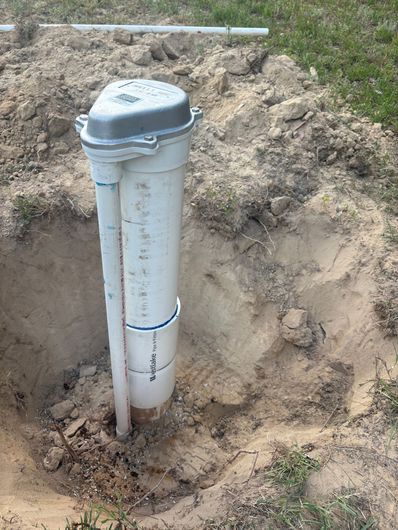 White utility pipe with vent cap installed in a dirt excavation outdoors