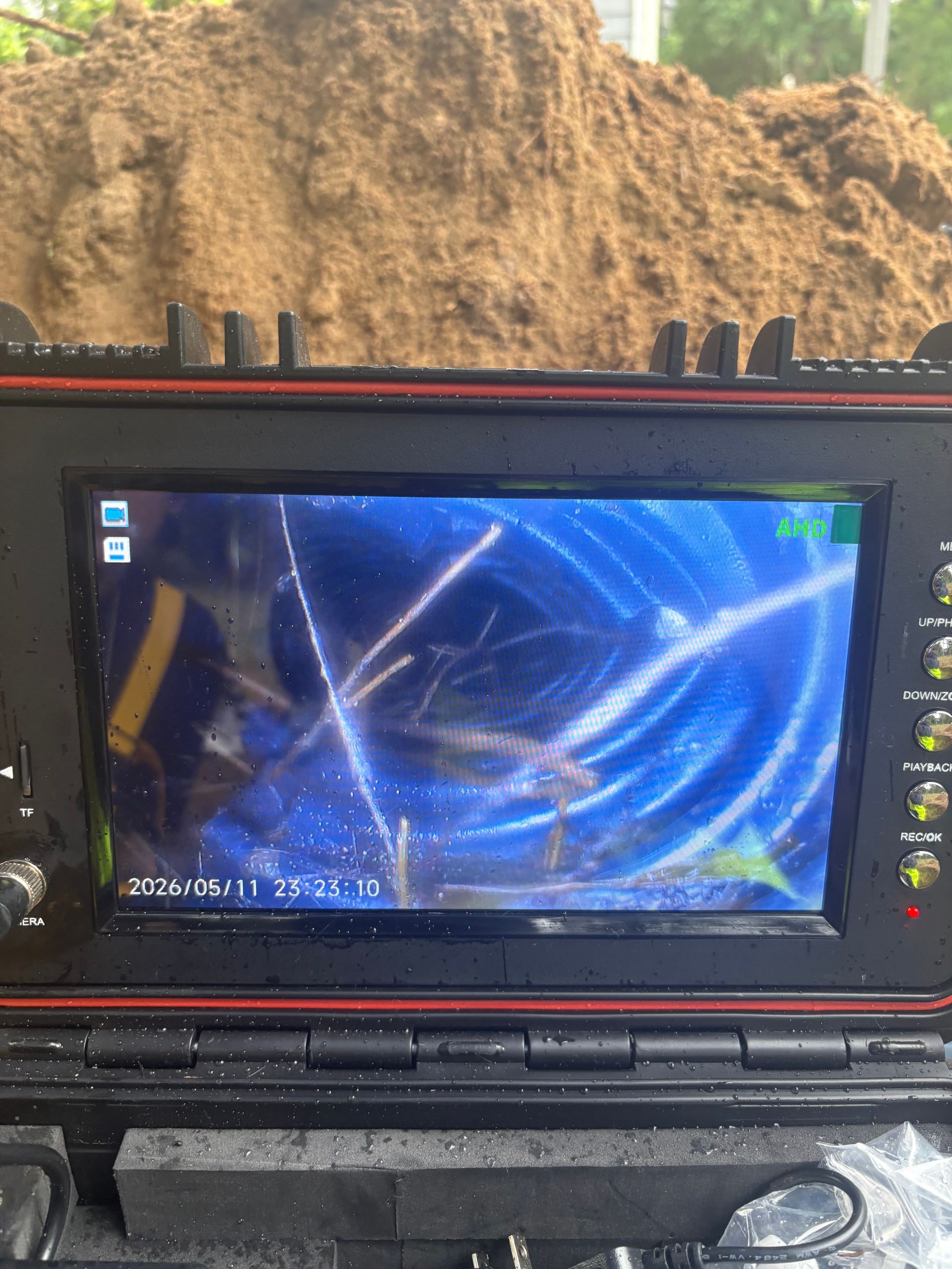 Rugged portable monitor showing a blue abstract display, mounted inside a vehicle on a rocky road.