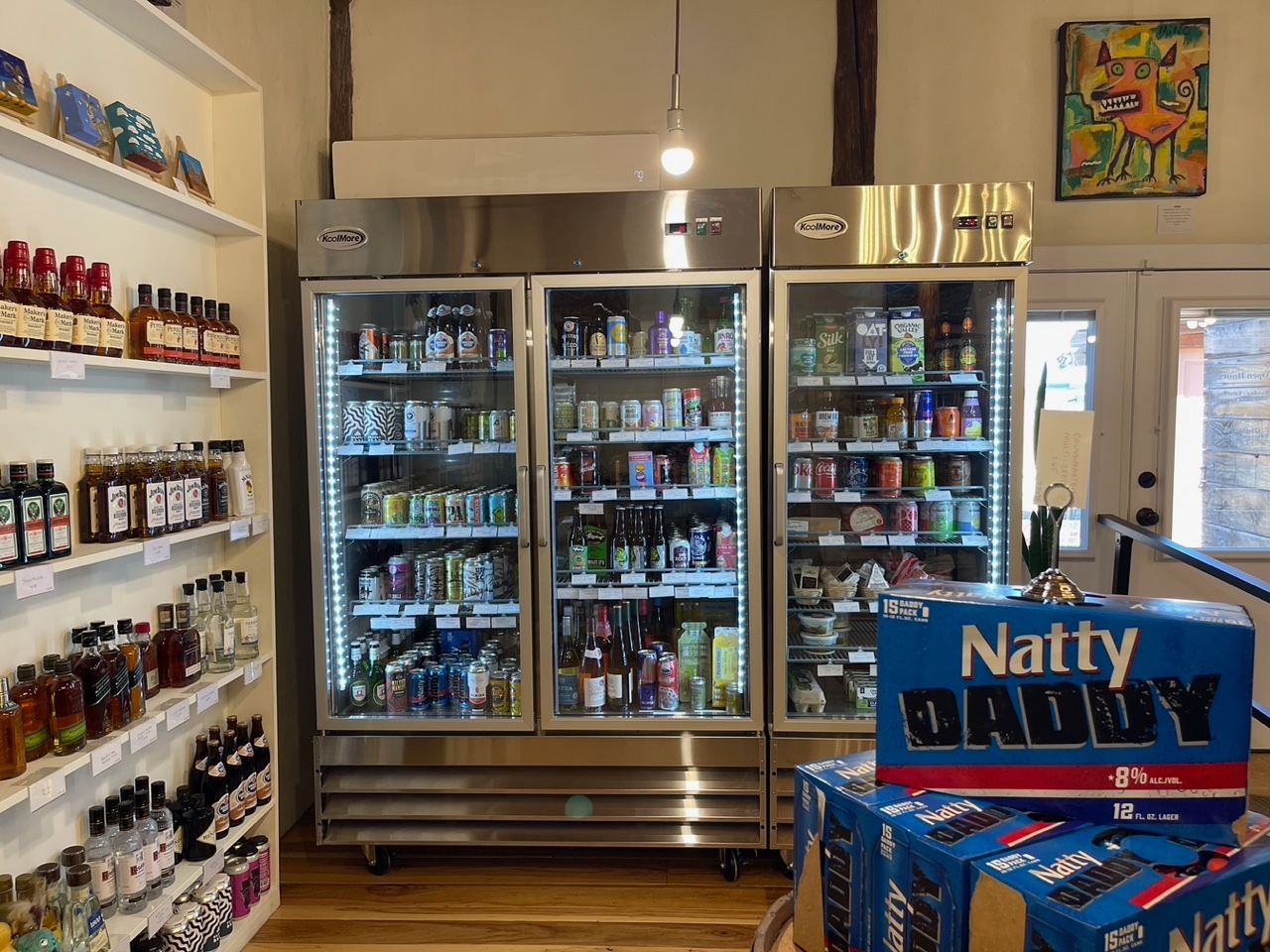 Convenience store aisle with refrigerated drinks, shelves of snacks, and beer display