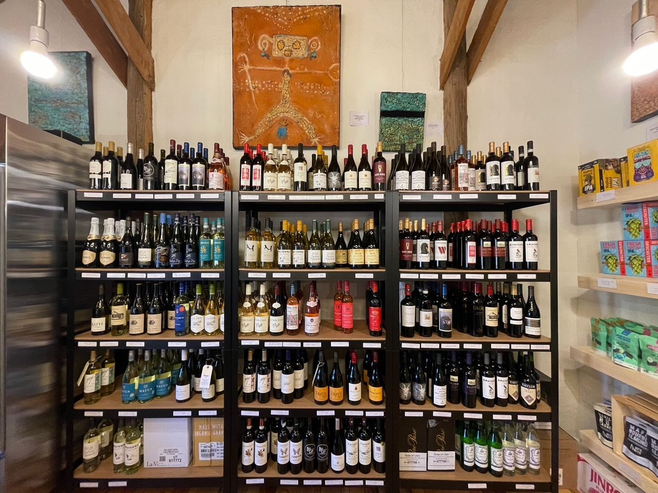 Shelves of assorted wine bottles in a small shop with bottles and snacks on the side