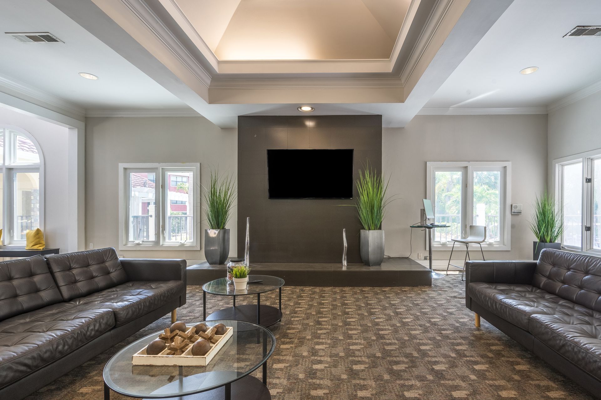 Modern clubhouse room with two black sofas, glass coffee table, and wall-mounted TV.