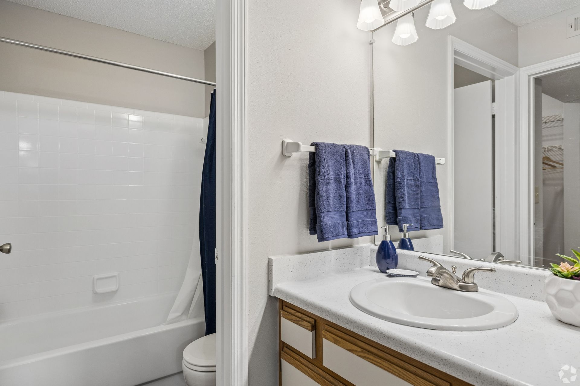 Bright bathroom with white tub, sink, mirror, and blue towels on the wall