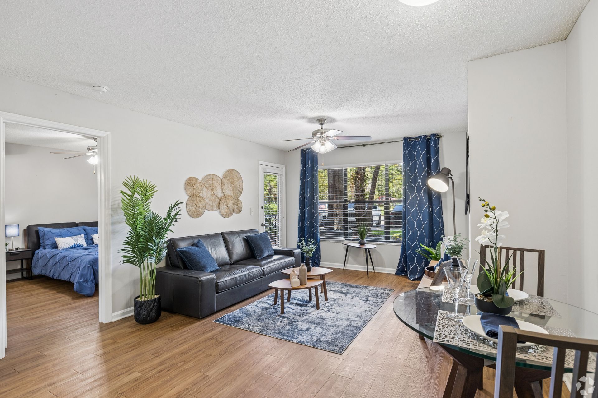 Bright living room with black sofa, blue rug, balcony doors, and dining table