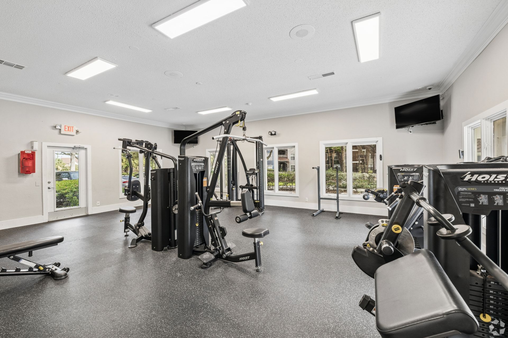 Bright gym interior with cable machines, benches, and large windows under white ceiling lights