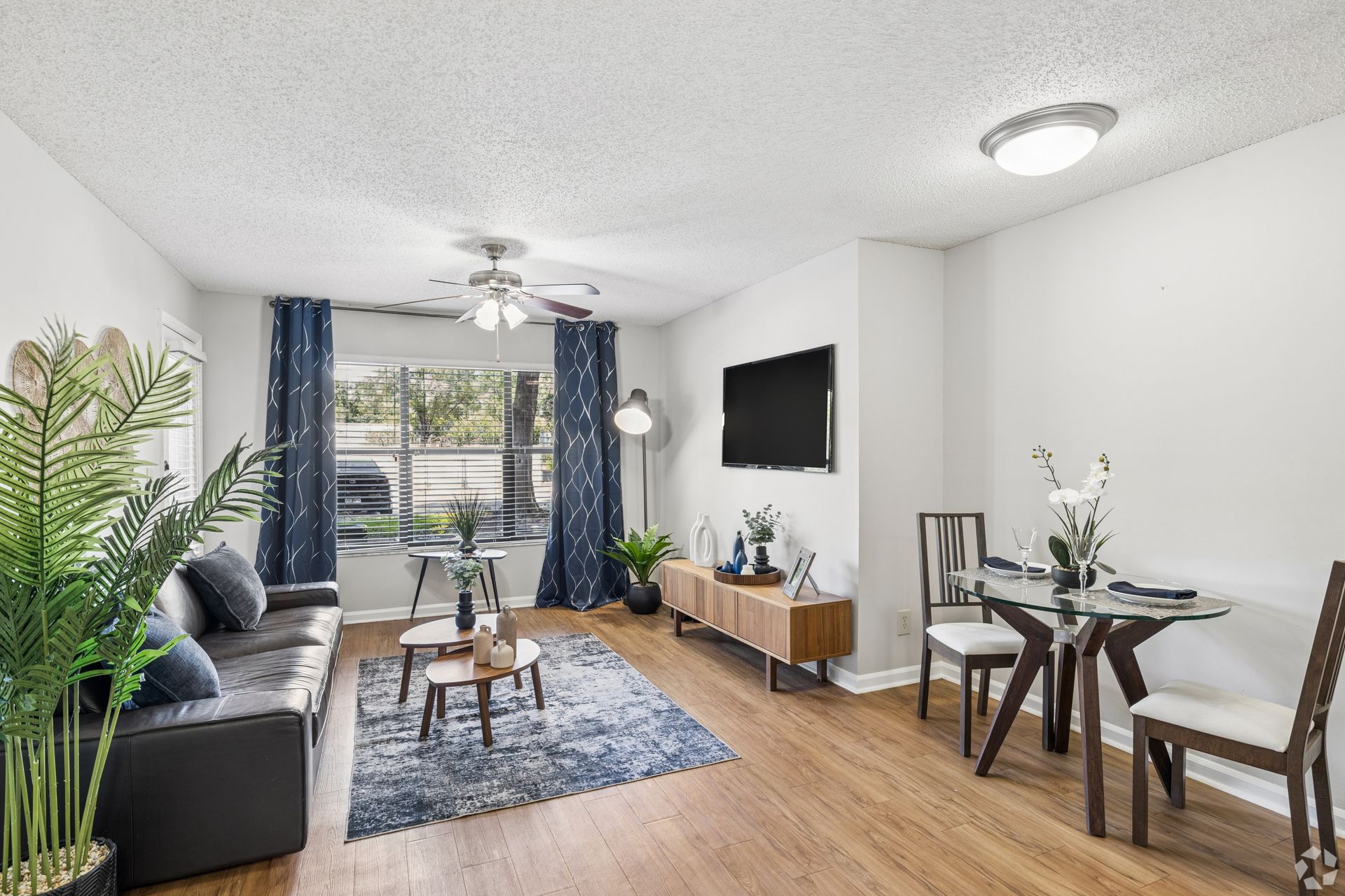 Modern living room with blue sofa, TV, dining nook, and balcony view