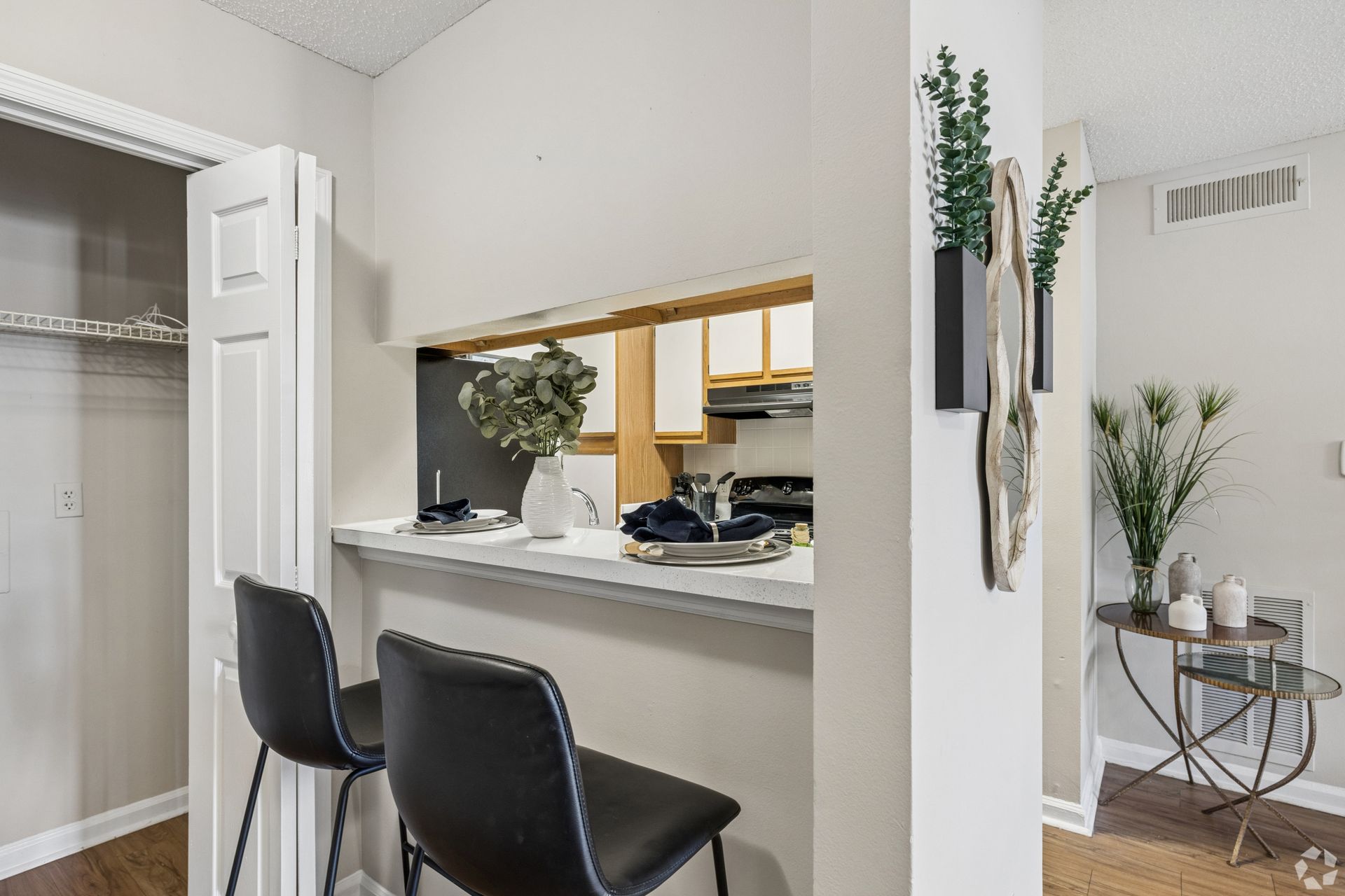 Bright modern apartment entryway with a breakfast bar, two black stools, and a closet; hallway with plant decor