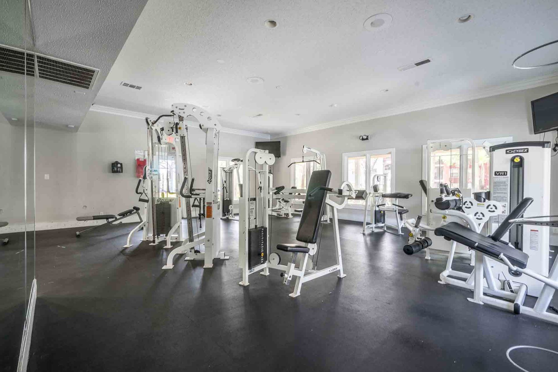 Empty modern gym with black flooring, white exercise machines, and mirrors along the back wall  | Grande Oasis at Carrollwood apartments for rent in Tampa, Florida.