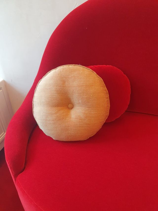 Deux coussins ronds, un beige et un rouge, sur un fauteuil courbé rouge vif.