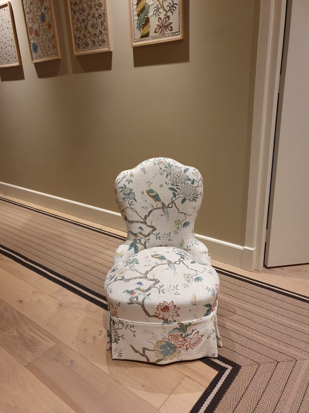 Petite chaise à imprimé floral dans un couloir, posée sur un tapis à motifs, avec une œuvre d'art encadrée sur le mur derrière.