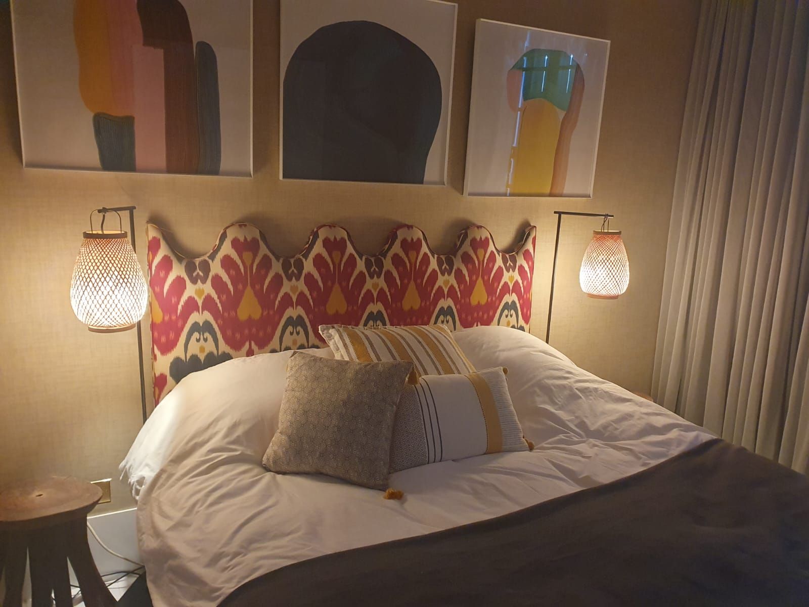 Chambre avec tête de lit à motifs, lit, coussins, œuvres d'art et appliques. Les murs sont neutres.