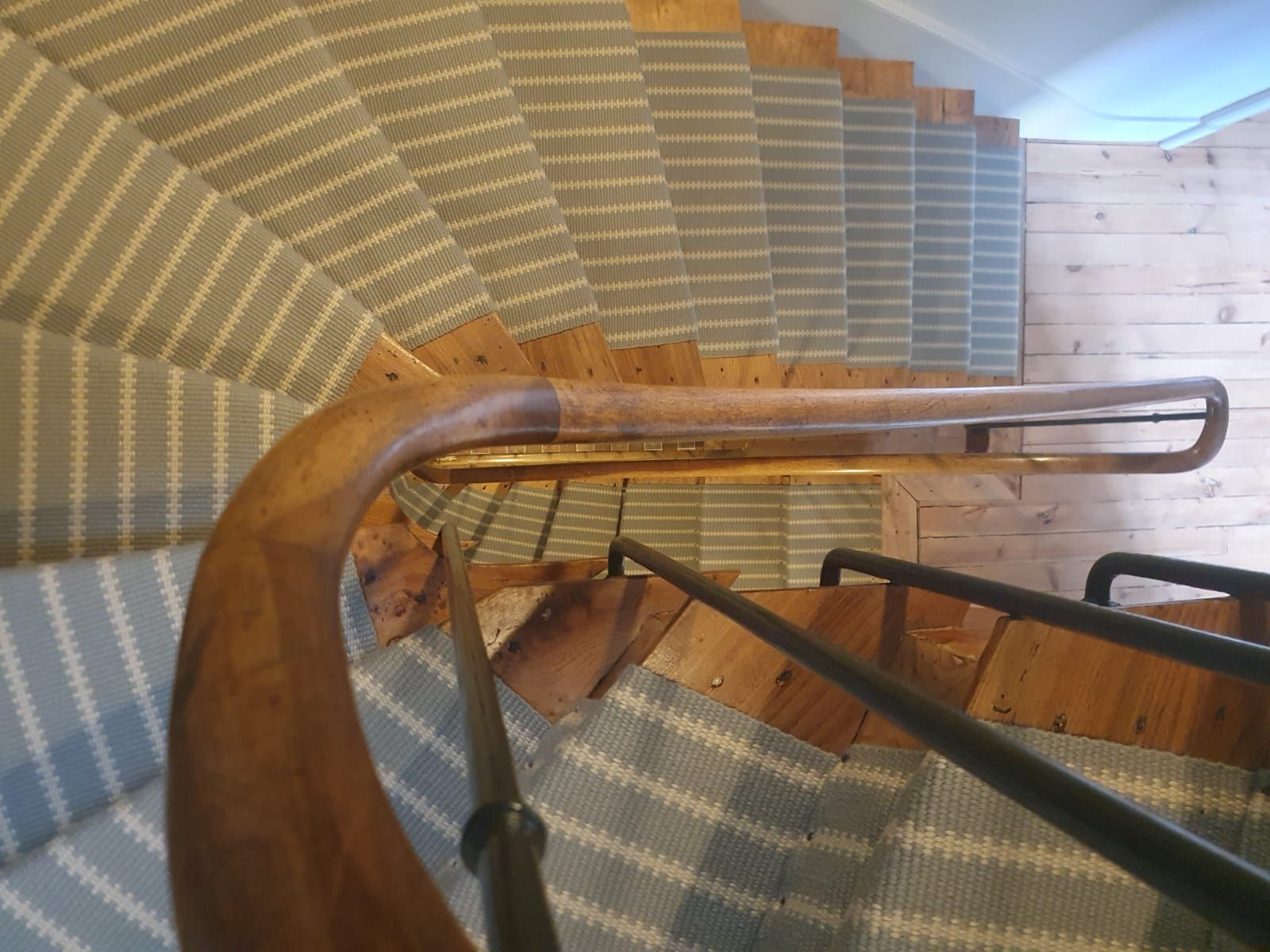 Vue aérienne d'un escalier en bois courbé avec un tapis rayé bleu clair et blanc et des rampes en bois.