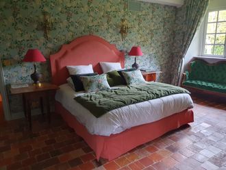 Chambre avec lit corail, papier peint fleuri, lampes rouges et canapé vert.