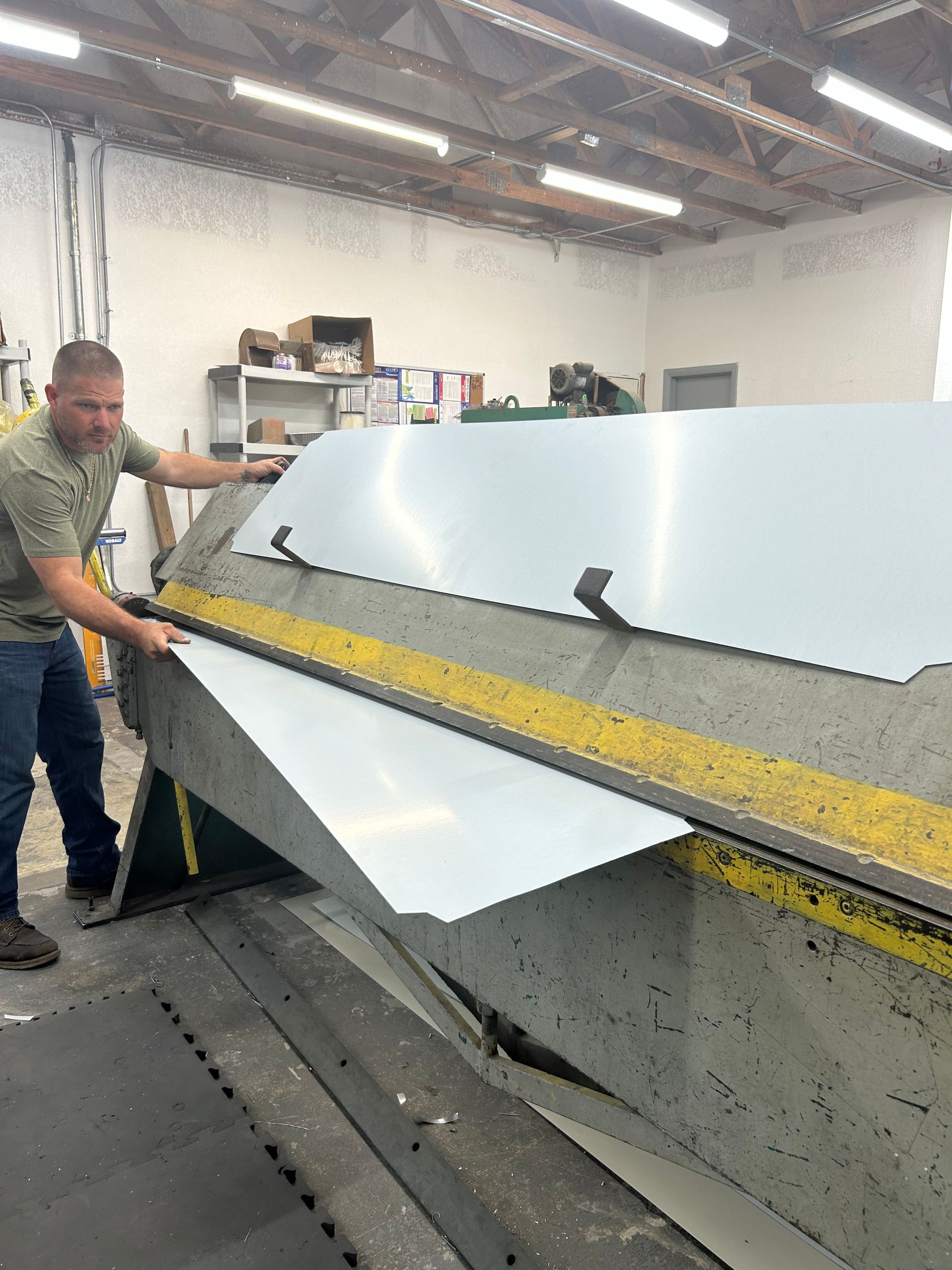 Man bending a large metal sheet on a machine in a workshop.
