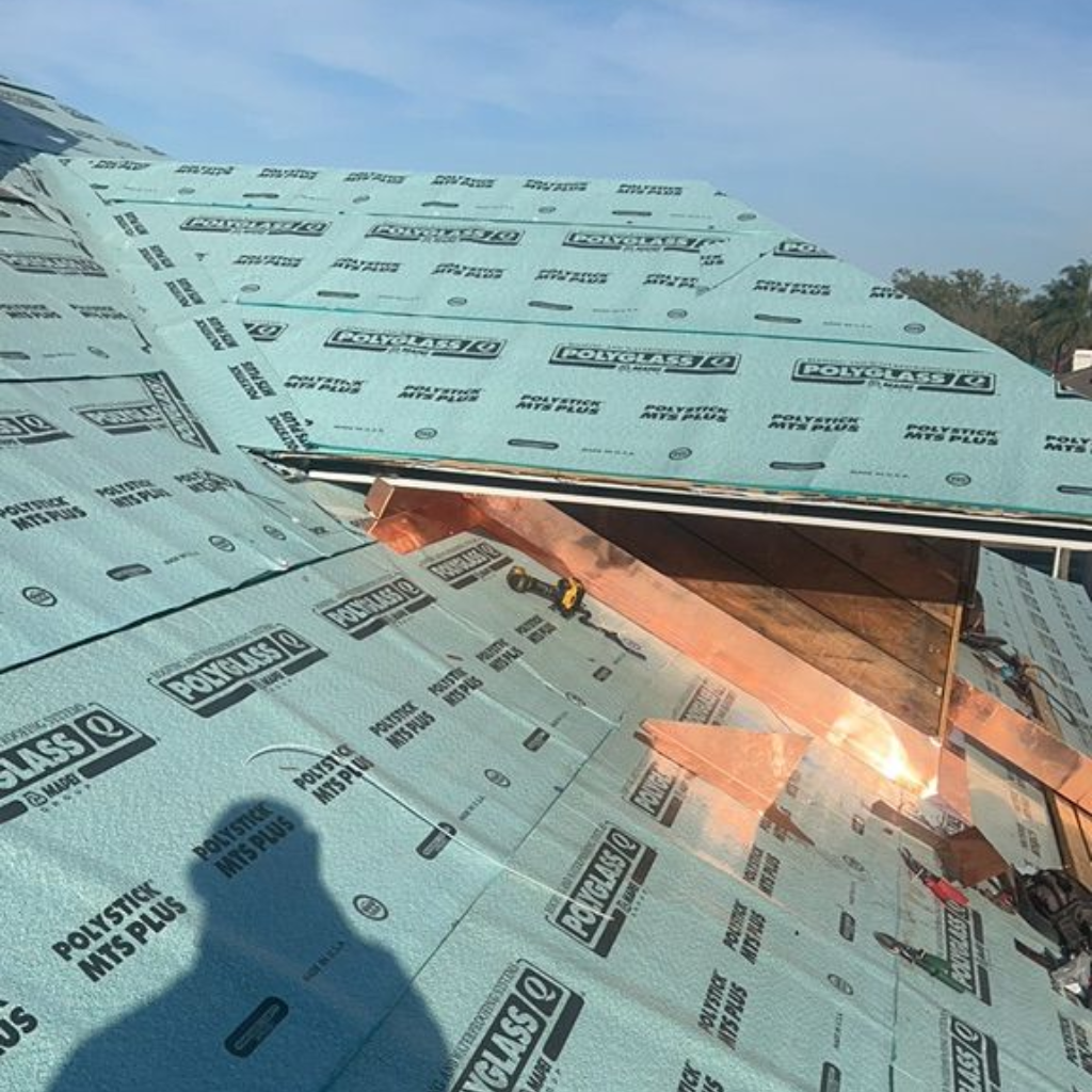 Rooftop under construction with turquoise underlayment and copper flashing, sunny day.