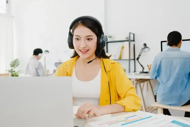 A woman in a pink sweater is holding a laptop computer and giving an ok sign.