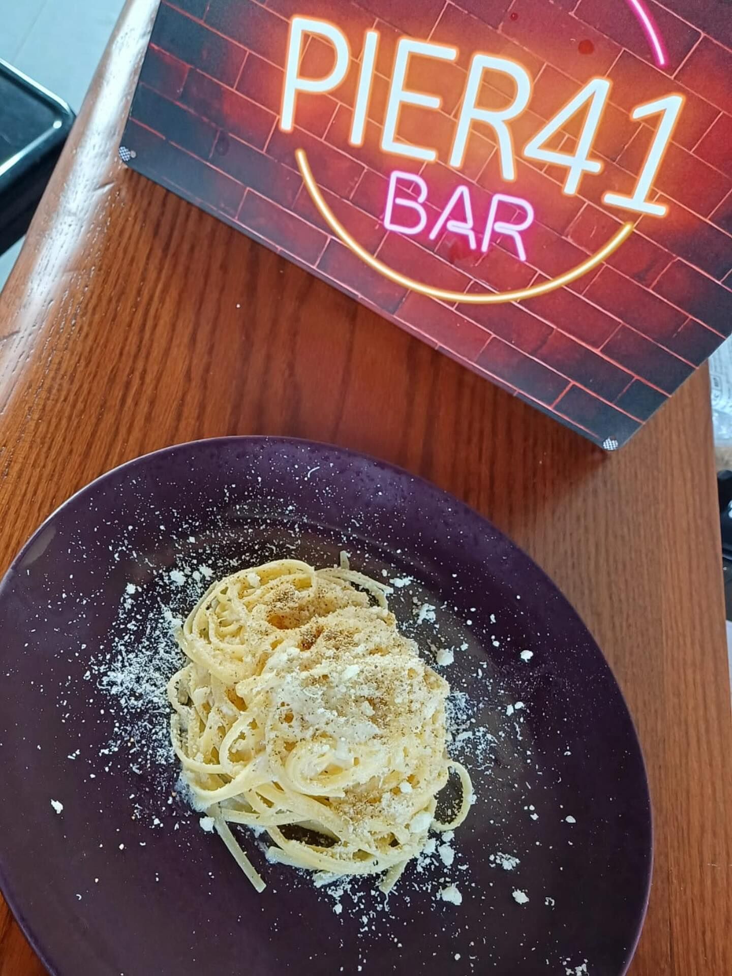 Un piatto di pasta con formaggio grattugiato sotto un'insegna al neon 