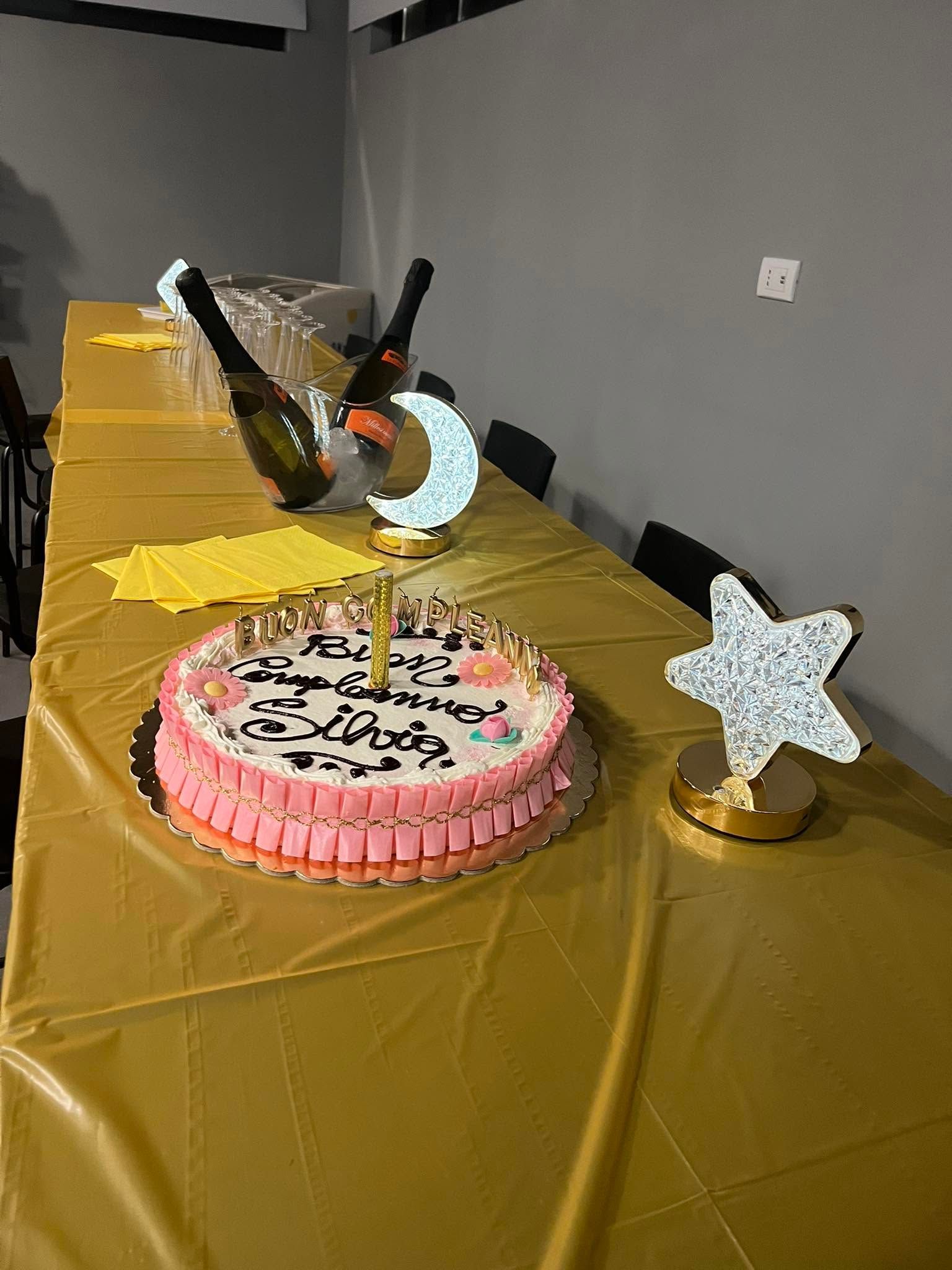 Torta di compleanno rosa su una tovaglia dorata con decorazioni a stella e scatoline per dolcetti in un allestimento per feste.