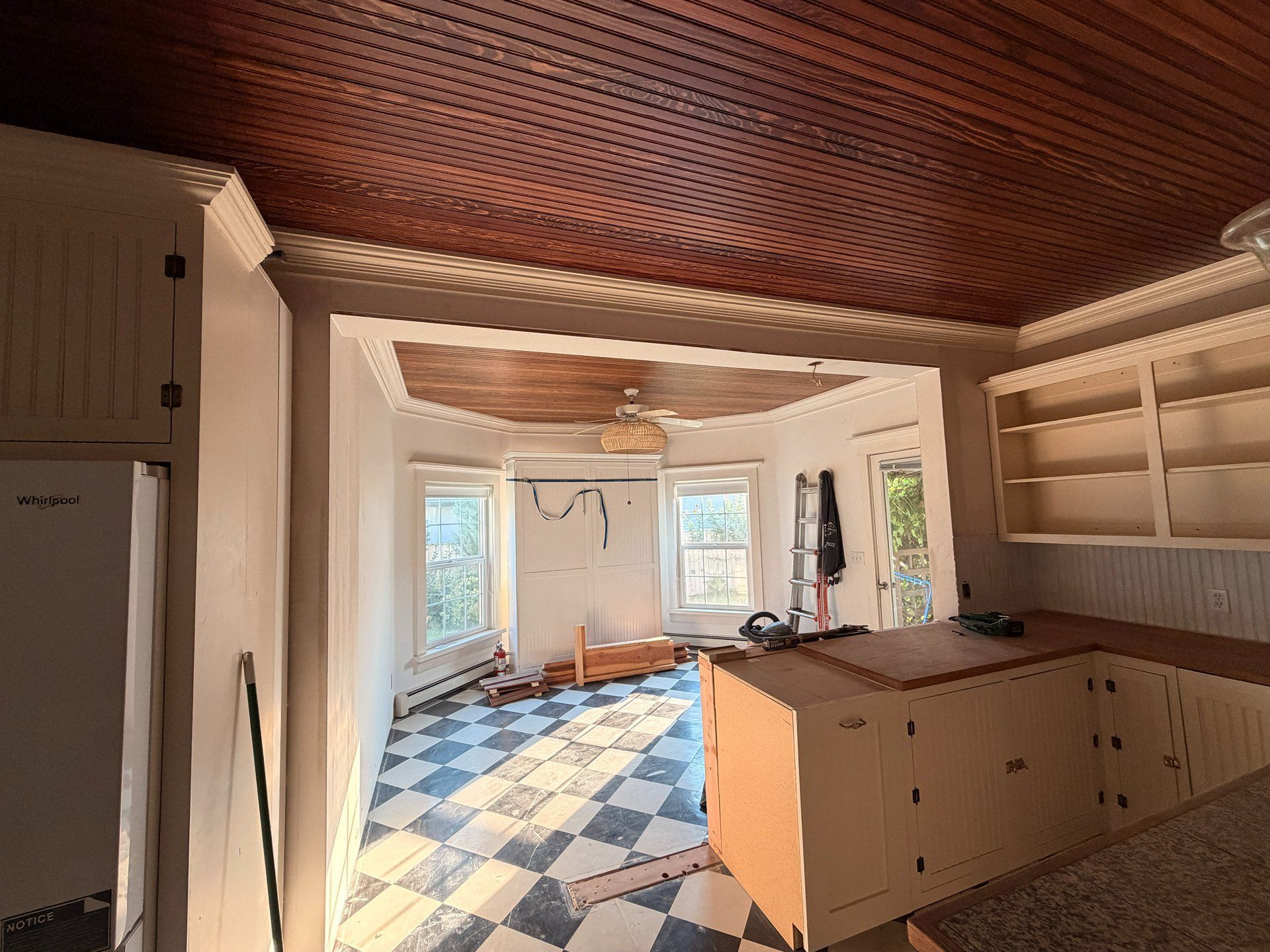 Bright empty kitchen with patterned tile floor, wood ceiling, and white cabinets by sunlit windows