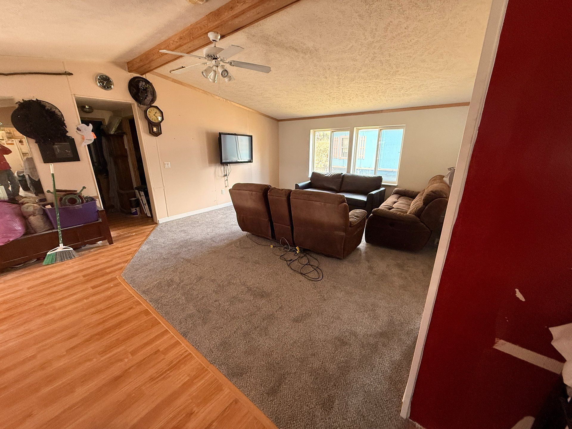 Living room with brown sofas, wall-mounted TV, carpeted seating area, and wood flooring near the entryway