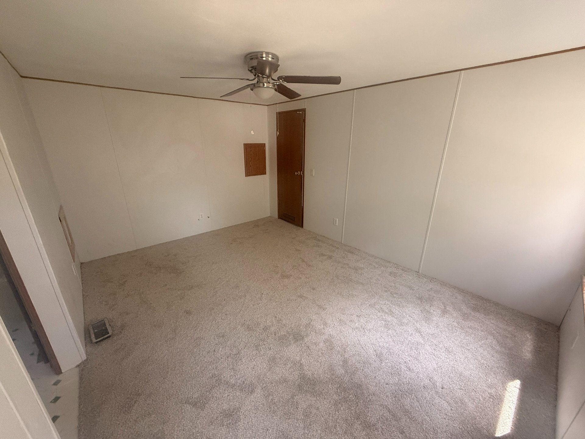 Empty beige bedroom with carpet, ceiling fan, and a wooden door