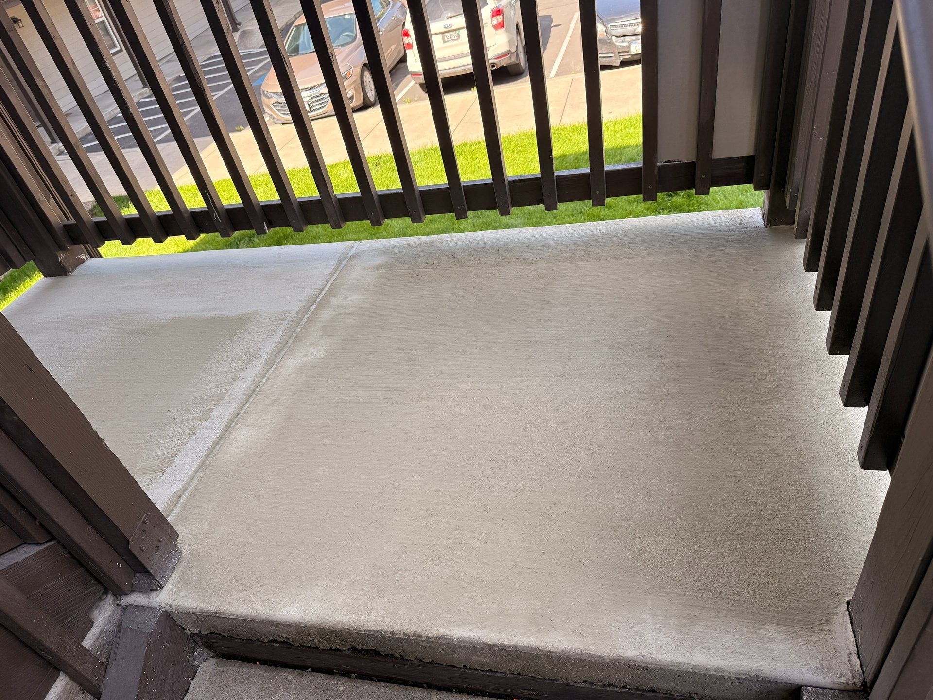 Concrete balcony floor with black railing overlooking a grassy area below