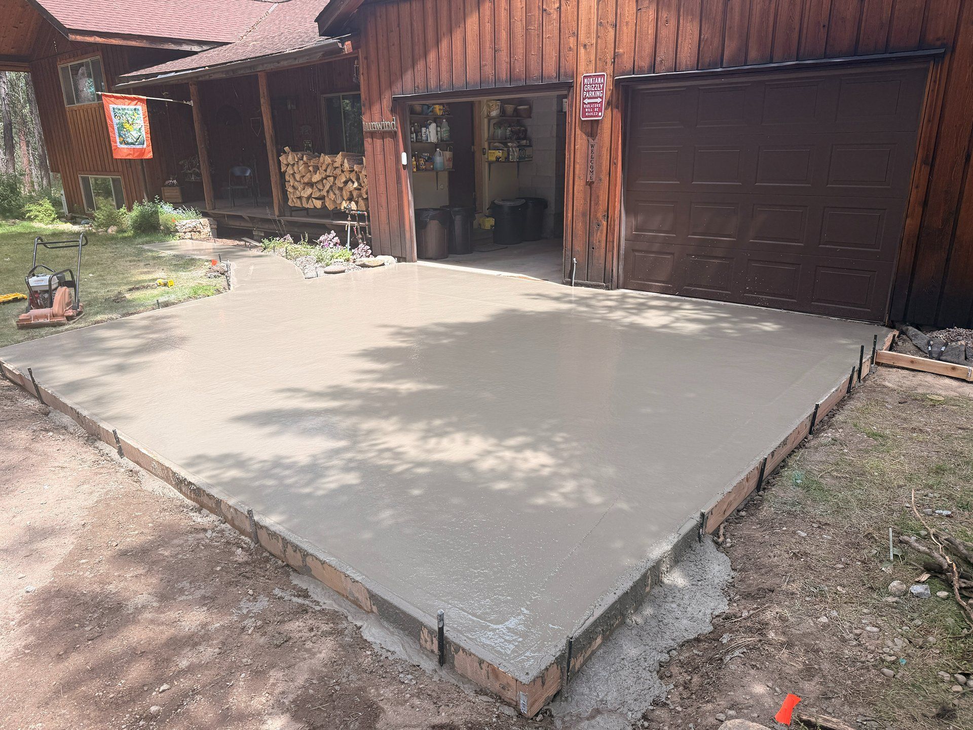 Freshly poured concrete slab in front of a rustic wooden building with a garage door.