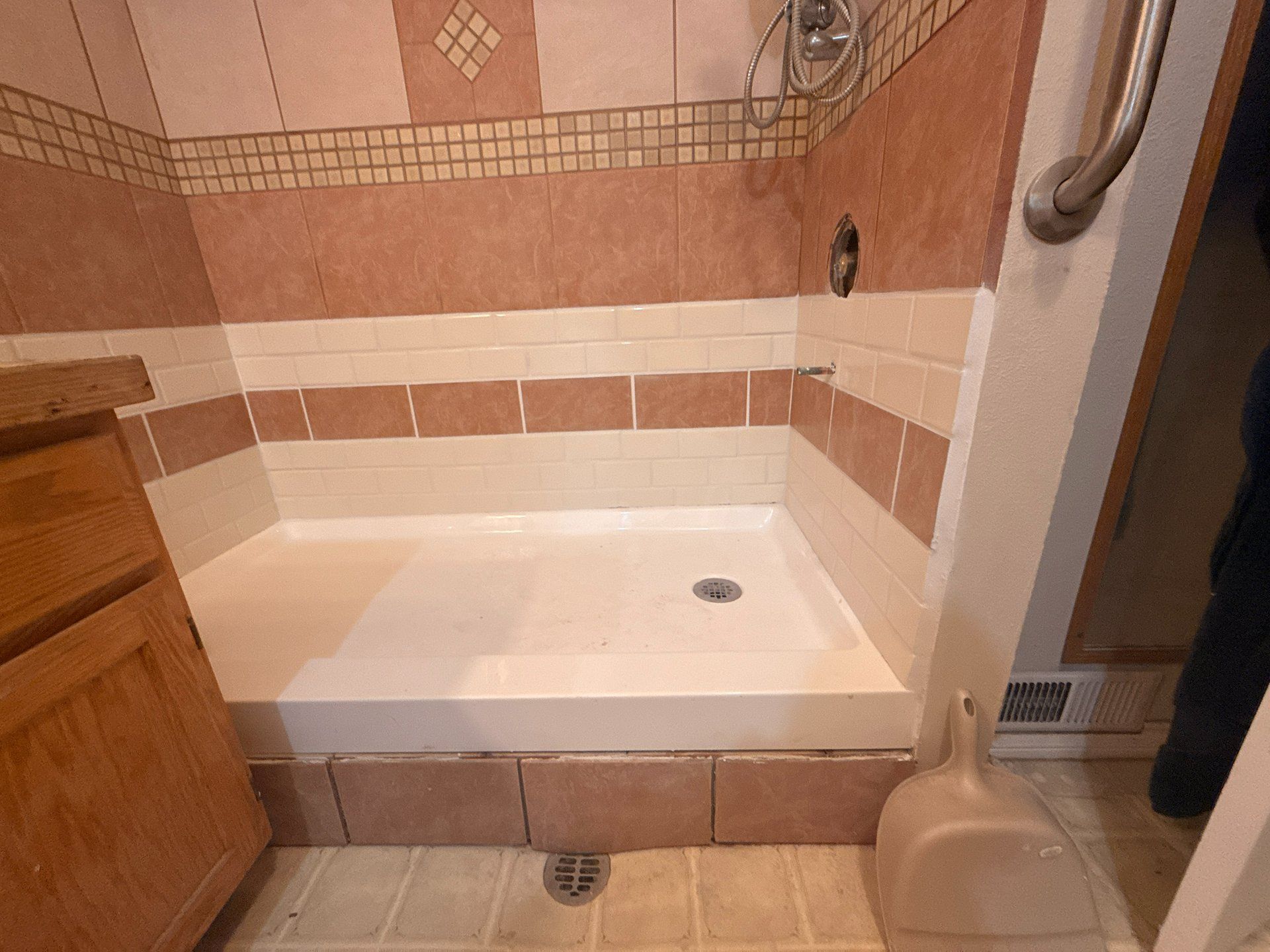 Walk-in shower with beige tile walls, a white tub base, and a handheld showerhead.