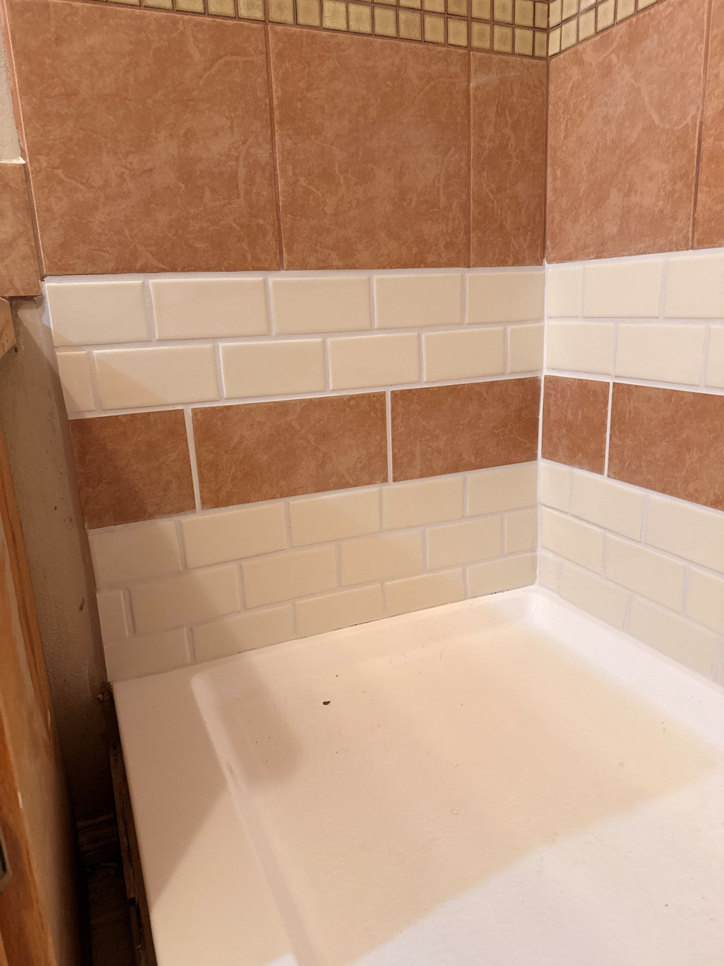 Small tiled shower stall with white and tan tiles and a white shower pan
