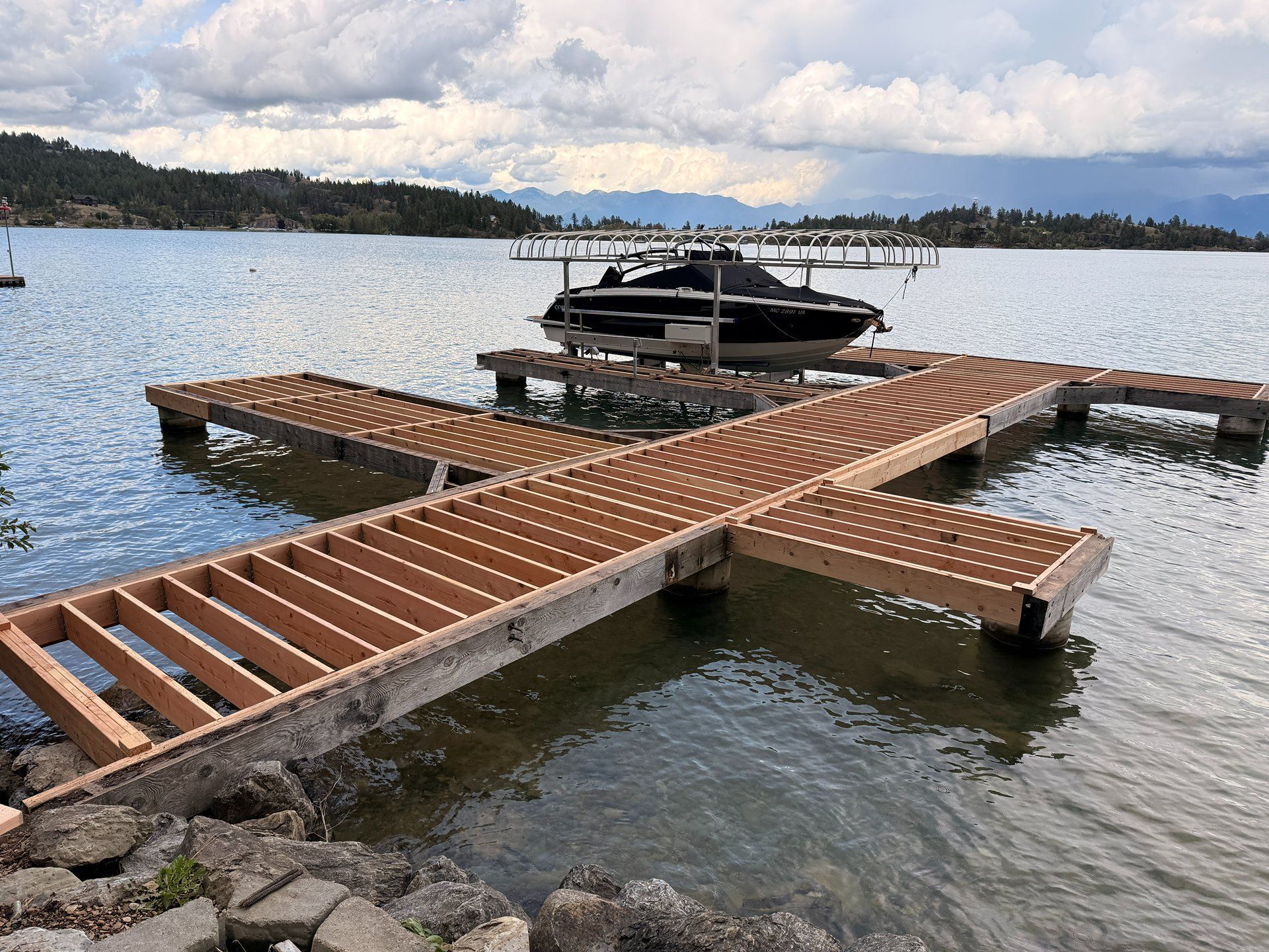 Wooden floating dock with a black boat on a lake under a cloudy sky