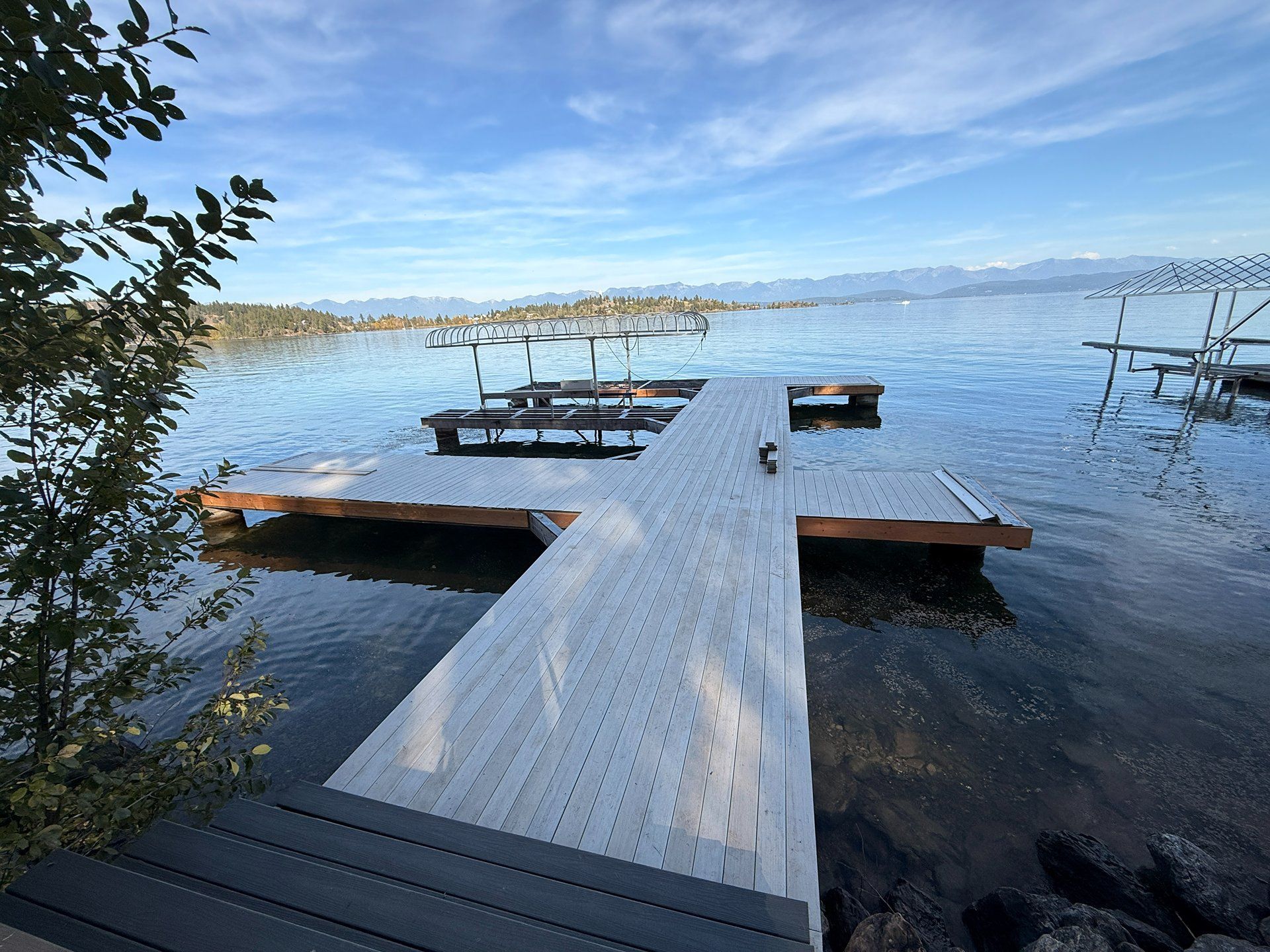 Wooden dock extending into a calm blue lake under a clear sky, with small floating platforms nearby