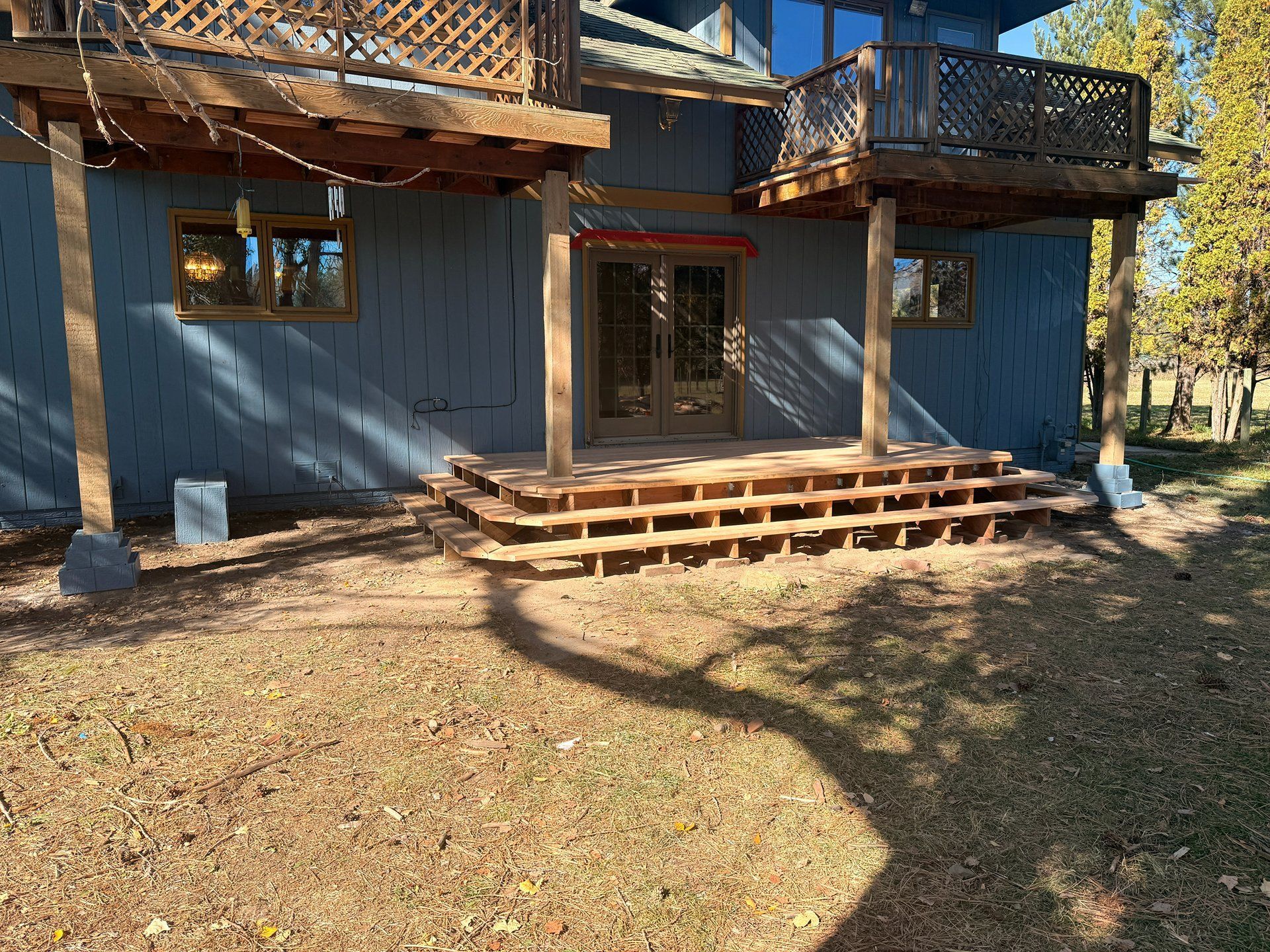 Wooden house exterior with blue siding, front steps, and wraparound balconies in a wooded yard
