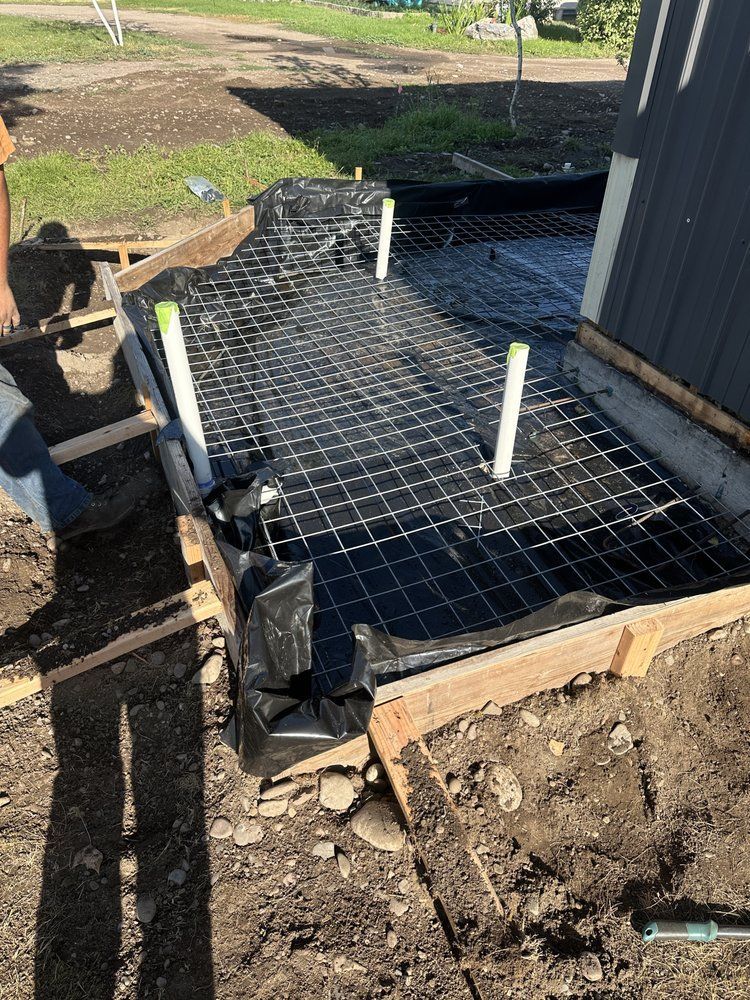 Black plastic-covered foundation footing with rebar grid and white PVC pipes at a construction site