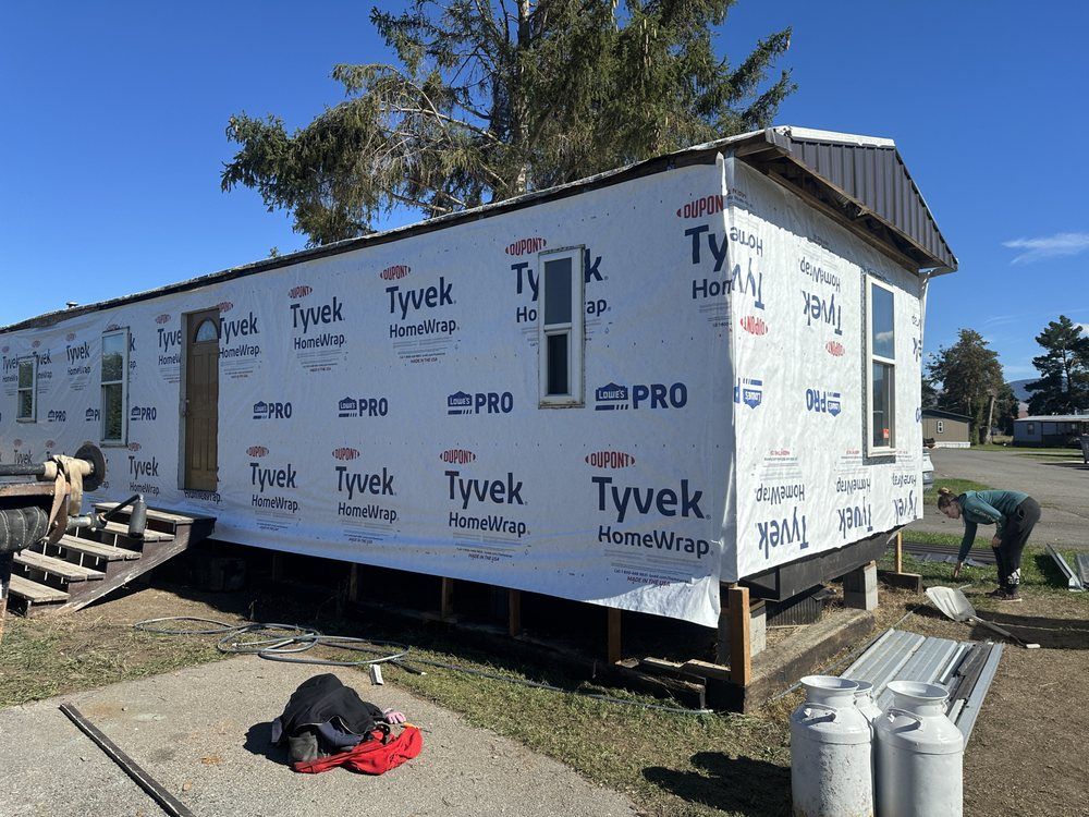 Tiny house under construction with Tyvek wrap, exposed foundation, and materials on a dirt lot