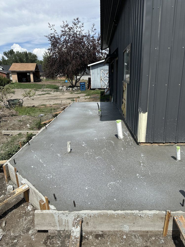 Fresh concrete walkway beside a dark gray building under construction, with forms and yard in the background