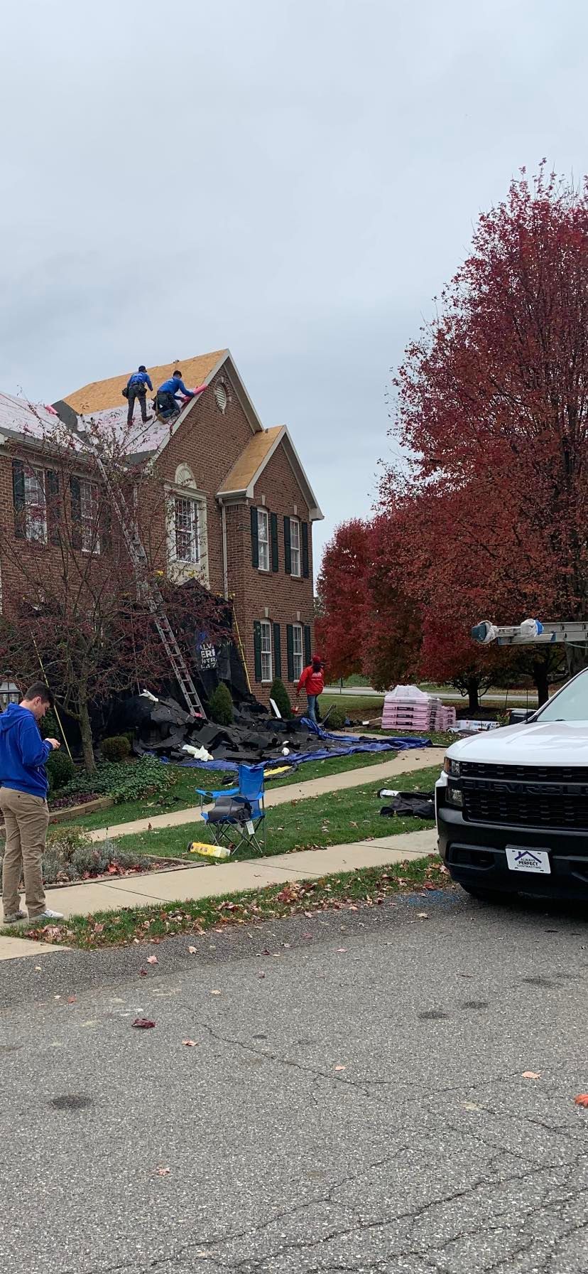 Roofers on a house with a ladder, tarps, and truck in a residential neighborhood.