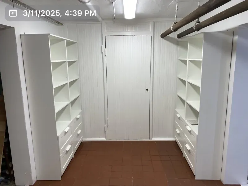 White shelves and drawers line a small room with a door in the center. Brown floor, white walls and ceiling.
