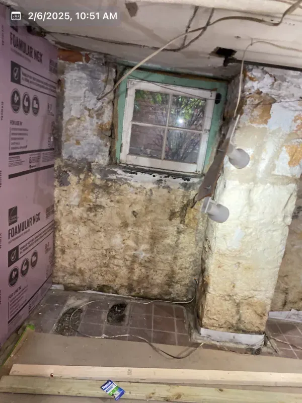 Basement with window, insulation, and water damage on the walls.