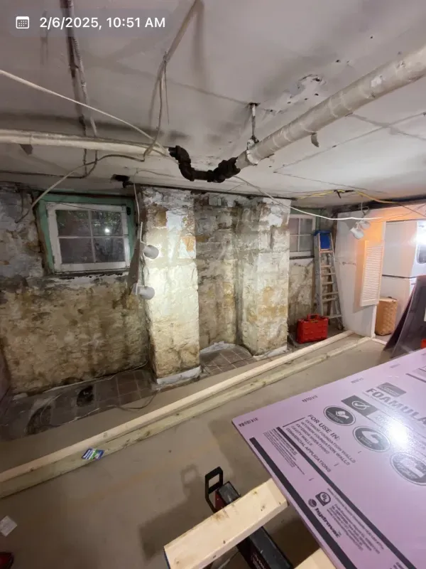 Basement interior with exposed brick, pipes, and insulation boards; construction in progress.