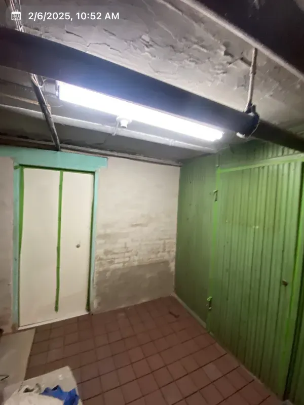 Basement room with a door, brick floor, and green paneling. A fluorescent light is mounted overhead.