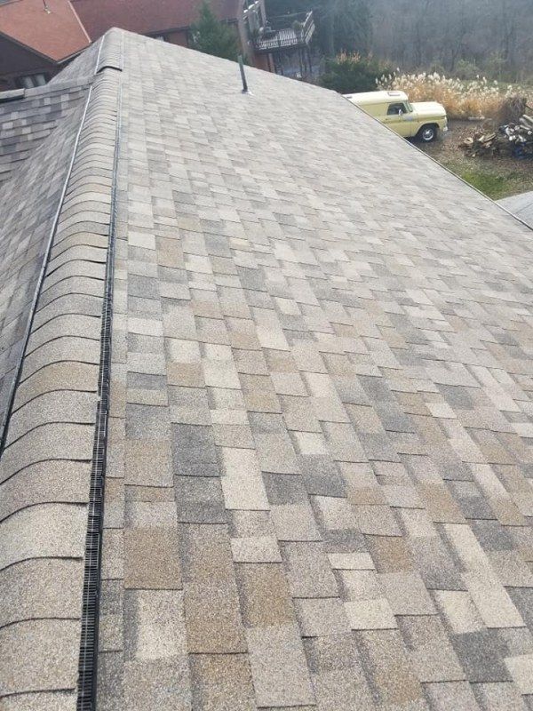 Close-up view of a shingled roof with various shades of gray, brown, and tan.
