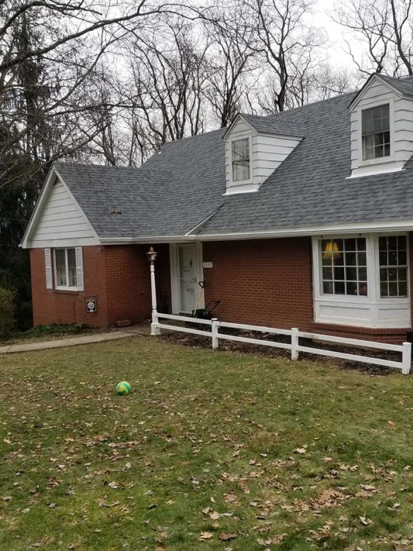 Brick house with gray roof, white trim, small yard, and a white picket fence.