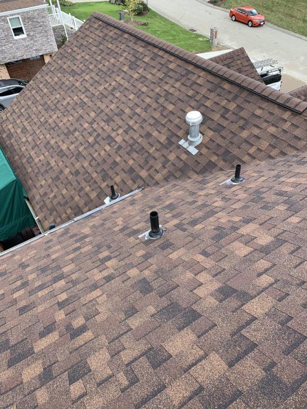 Brown asphalt shingle roof with vents. A car and buildings are in the background.