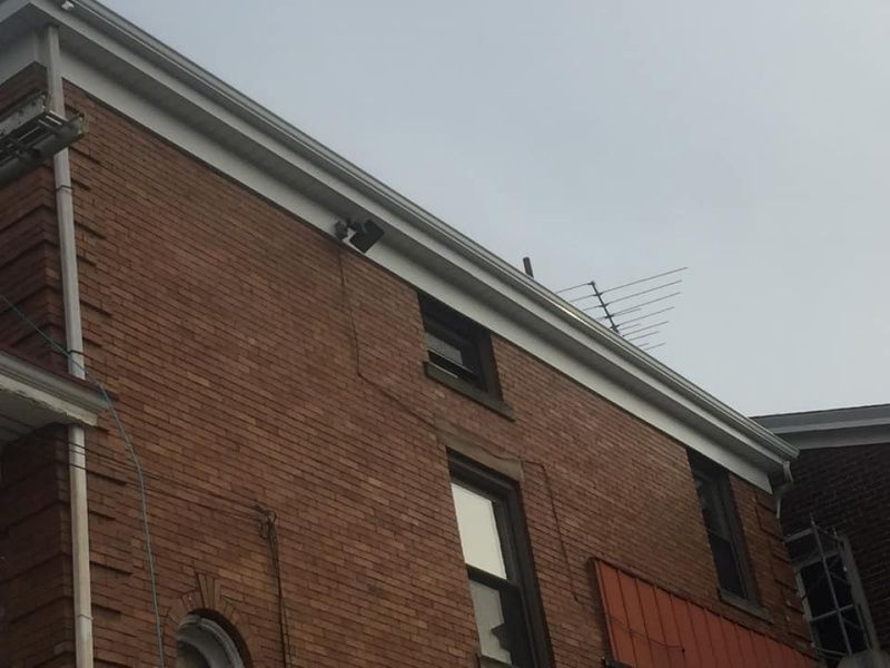 Red brick building exterior with white trim, gray sky. Windows and an antenna are visible.