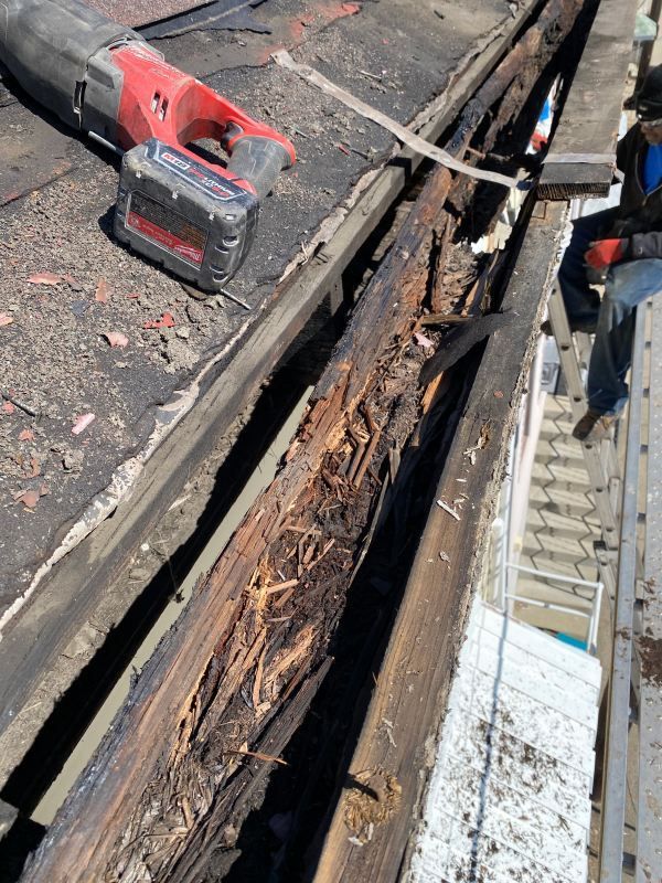 Damaged roof gutter being repaired, with power saw and wood debris visible.