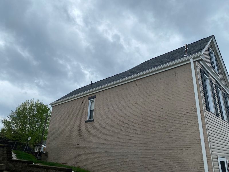 Tan brick building with a dark roof and white trim under an overcast sky.