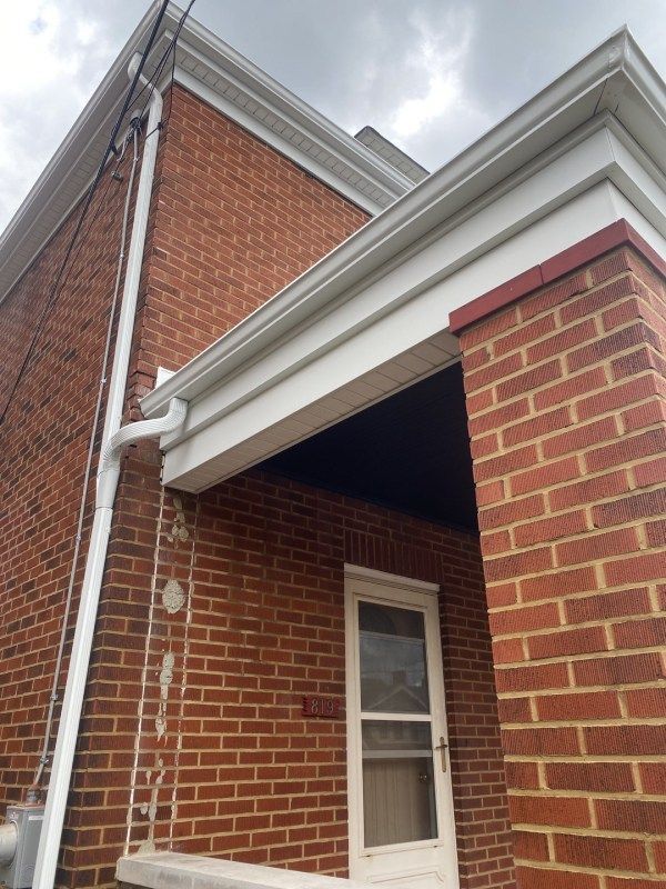 Red brick building with white trim, gutters, and a door under a porch roof. Overcast sky.